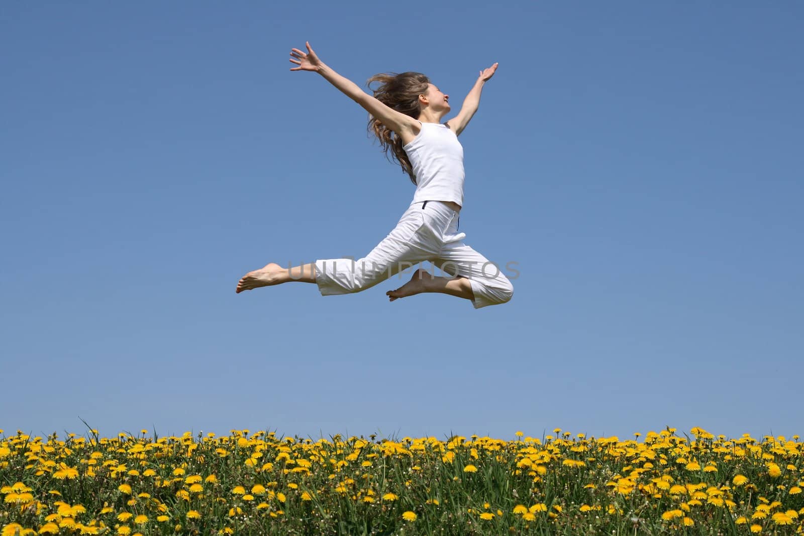 Girl in summer white clothes flying in a jump over flowering dandelion field.