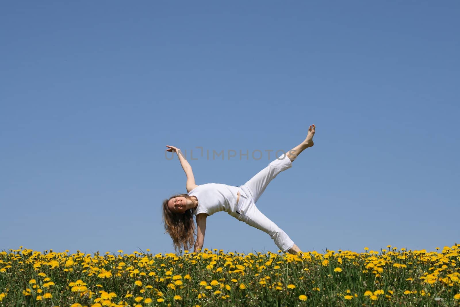Smiling young woman exercising in dandelion field by anikasalsera