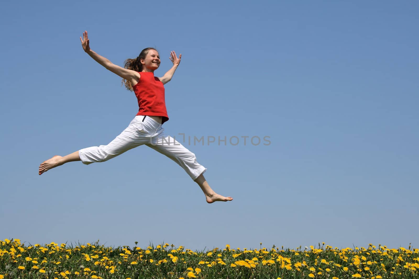 Girl in red t-shirt flying in a jump over flowering dandelion field.
