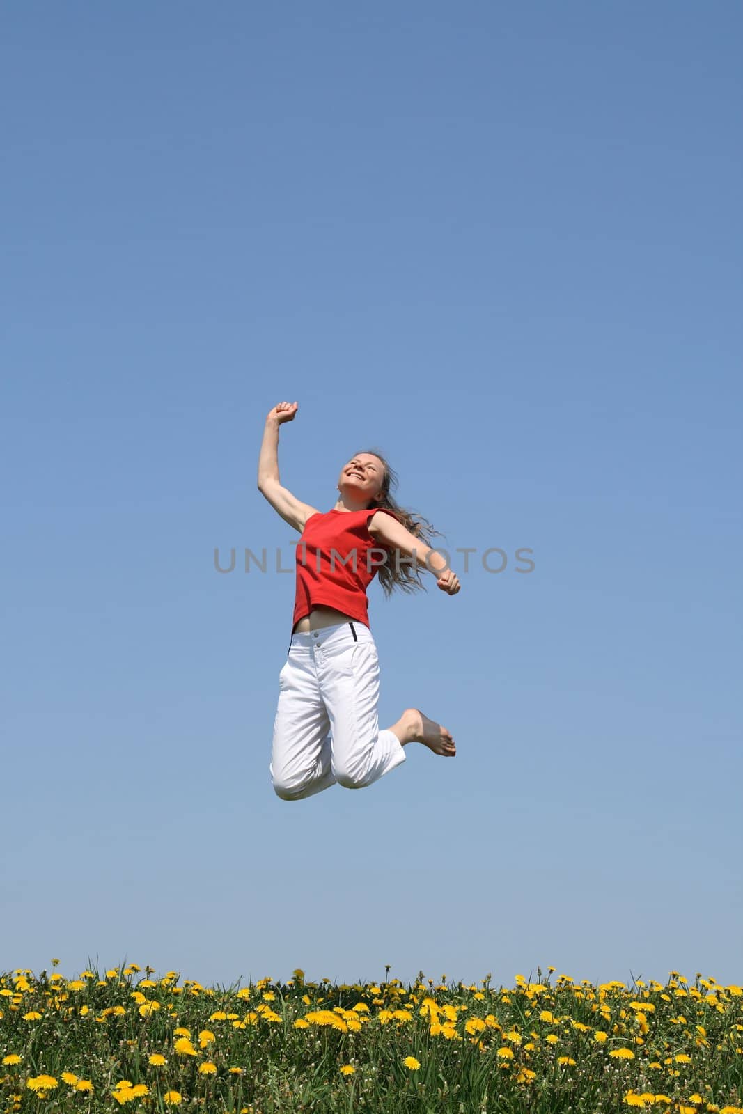 Smiling happy girl jumps in flowering dandelion field.