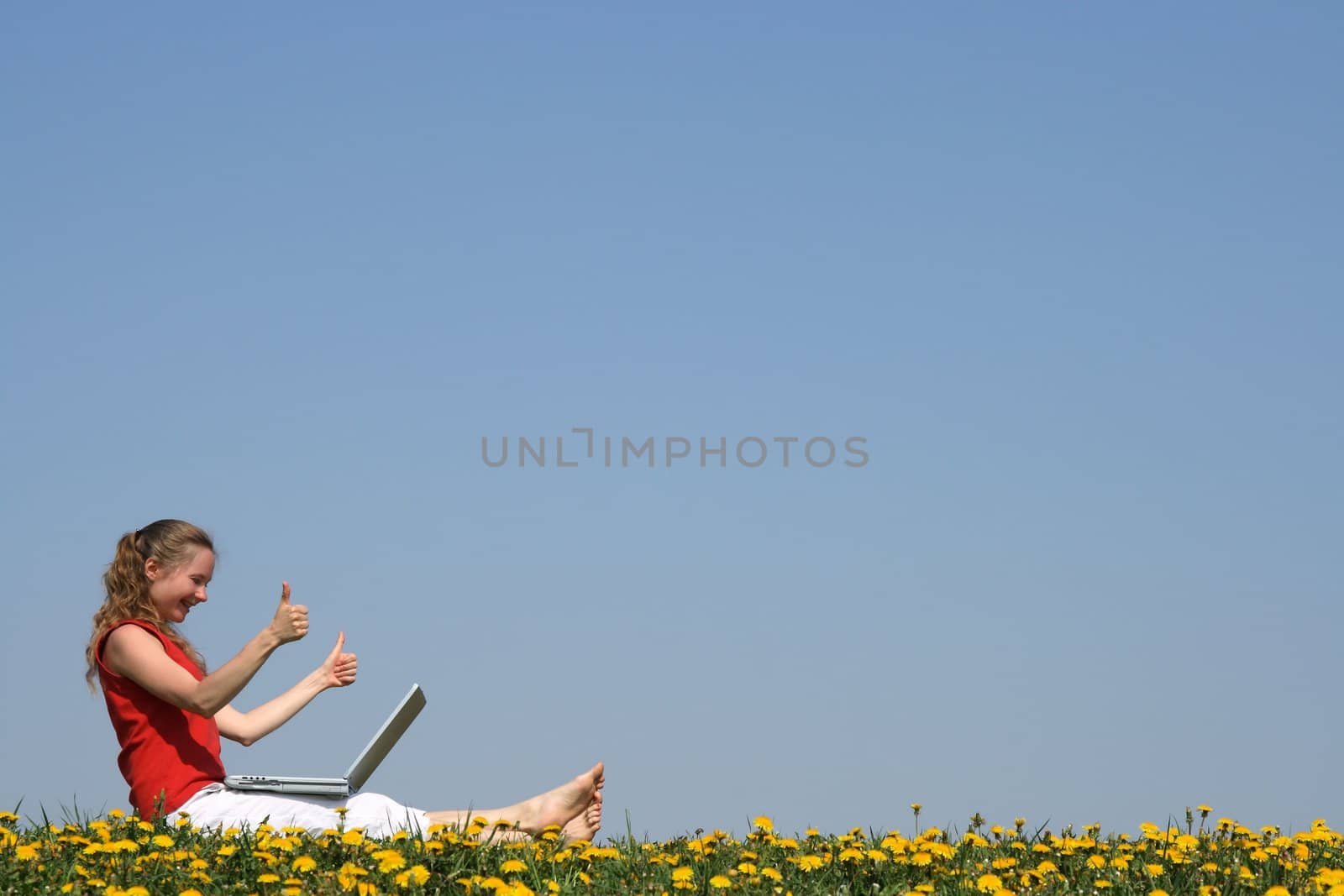 Thumbs up! Smiling girl with laptop in a flowering field.