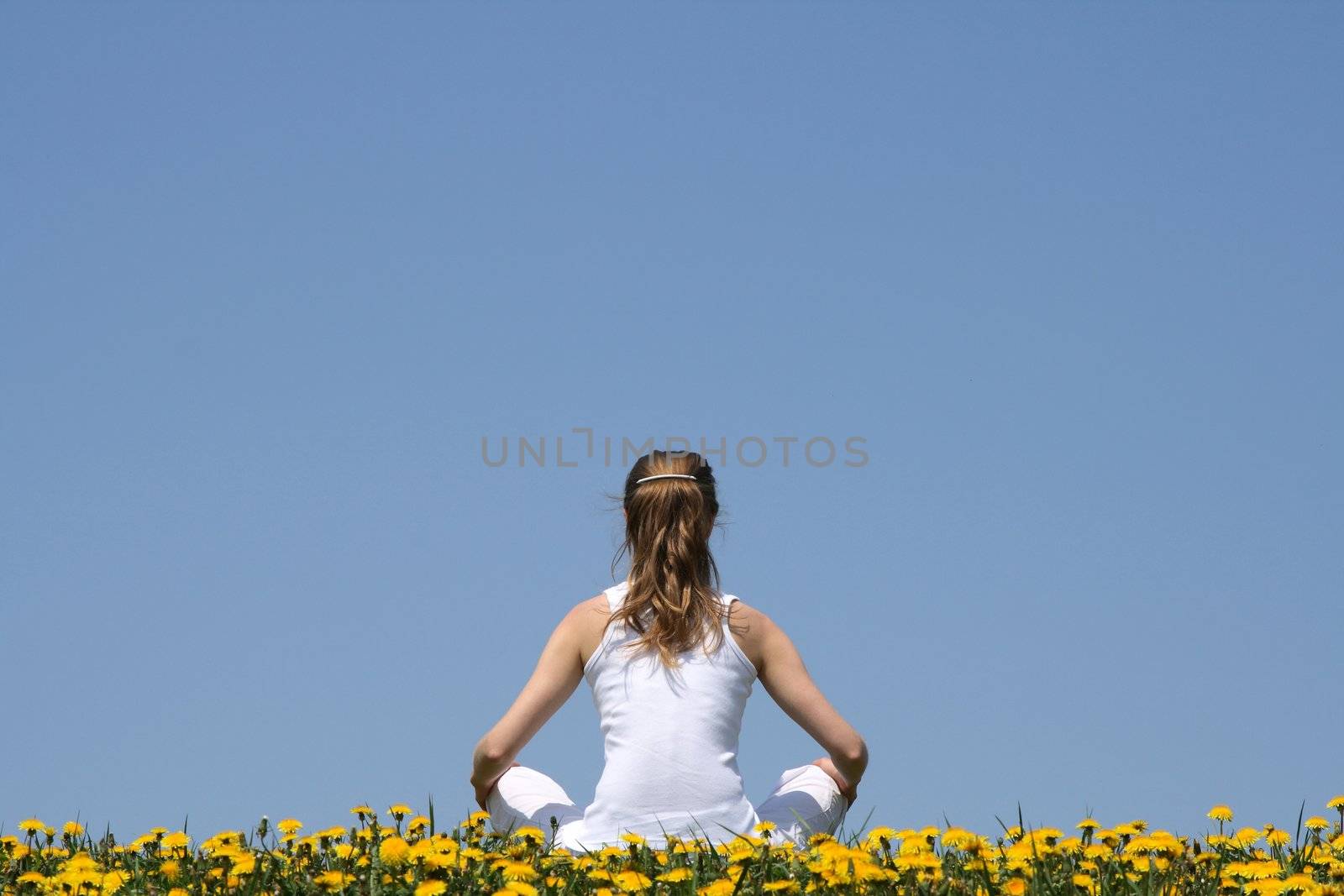 In harmony with nature. Young woman in white clothes sitting in a flowering dandelion field.