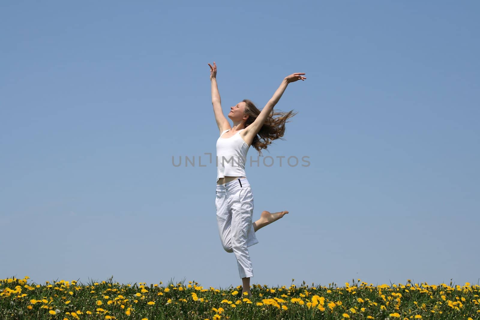 Natural beauty. Young woman in summer white clothes dancing in a flowering field.