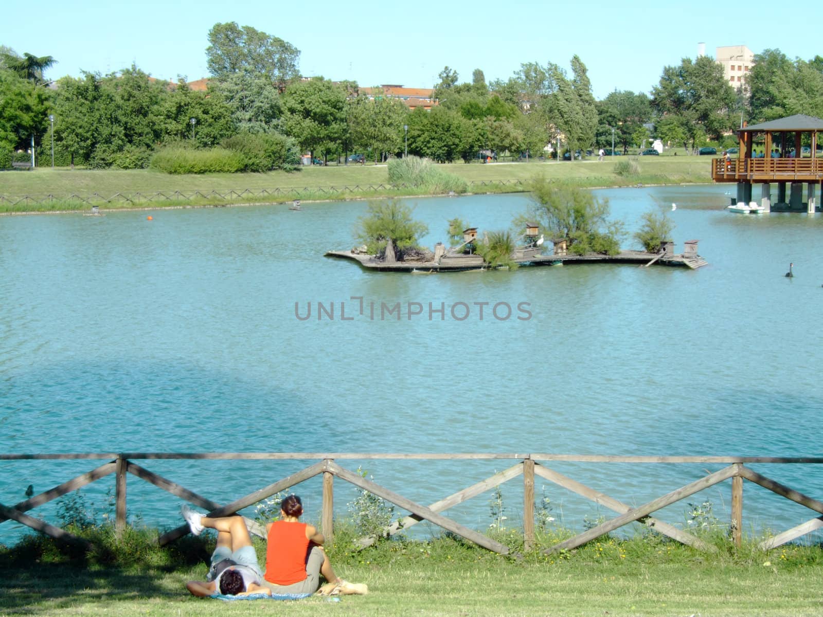 Young couple relaxing on the grass in the park, in front of the lake