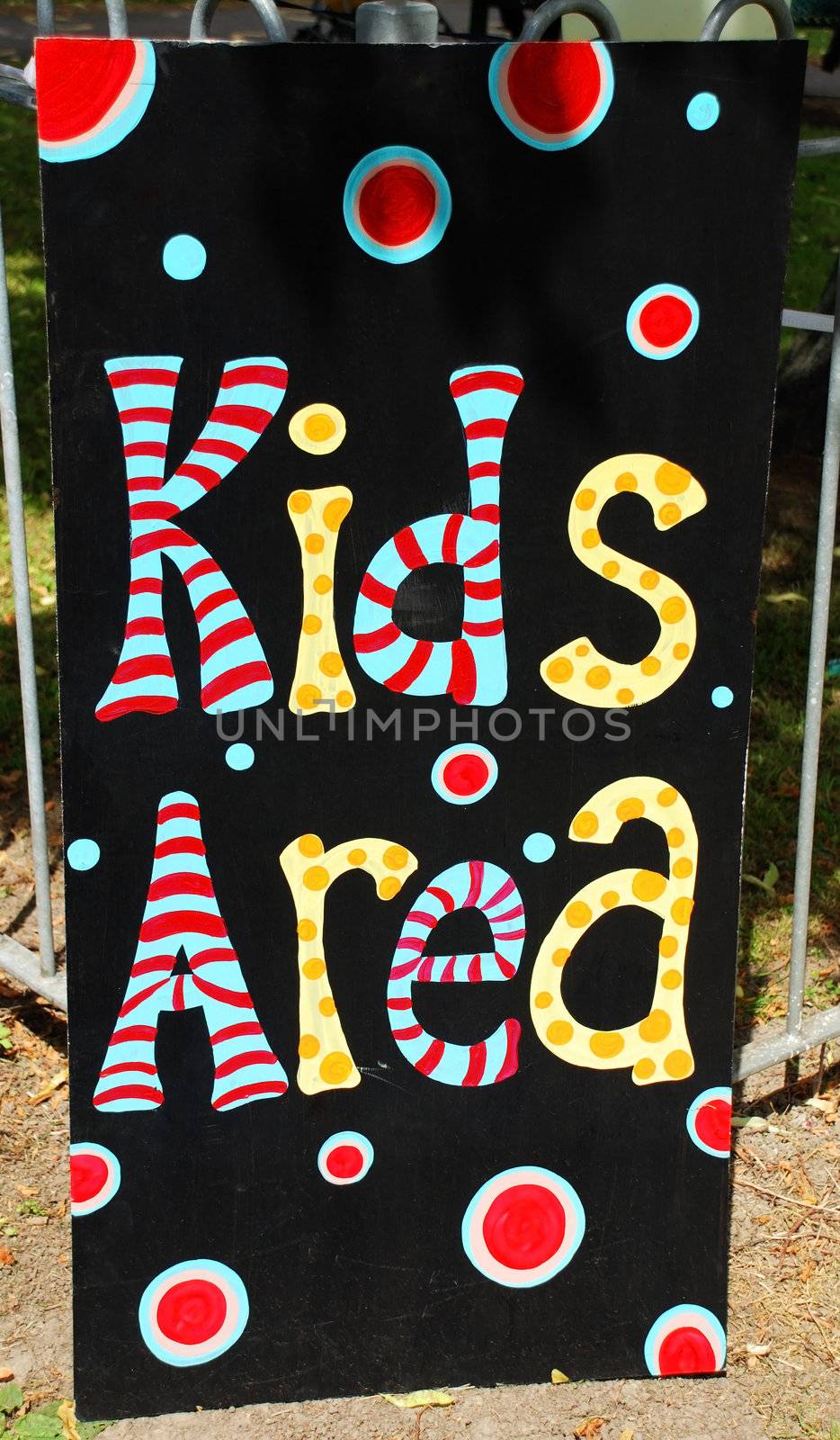 A photograph of a sign for a 'kids' area', situated outdoors in front of the fence around a play park