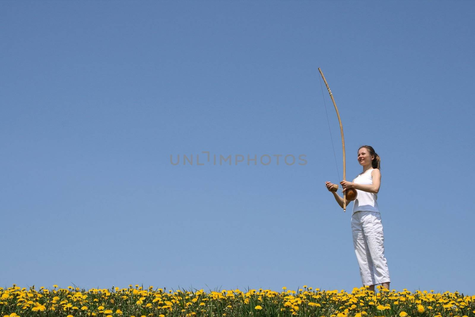 Girl playing berimbau (traditional Brazilian music instrument) in flowering spring meadow.
