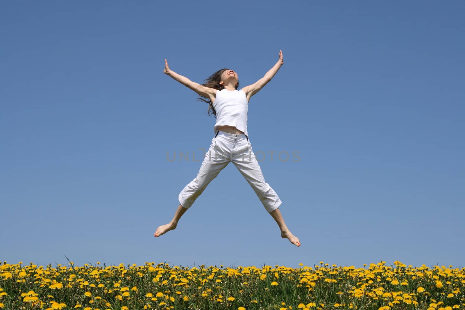 Smiling girl in summer white clothes jumping in flowering meadow.