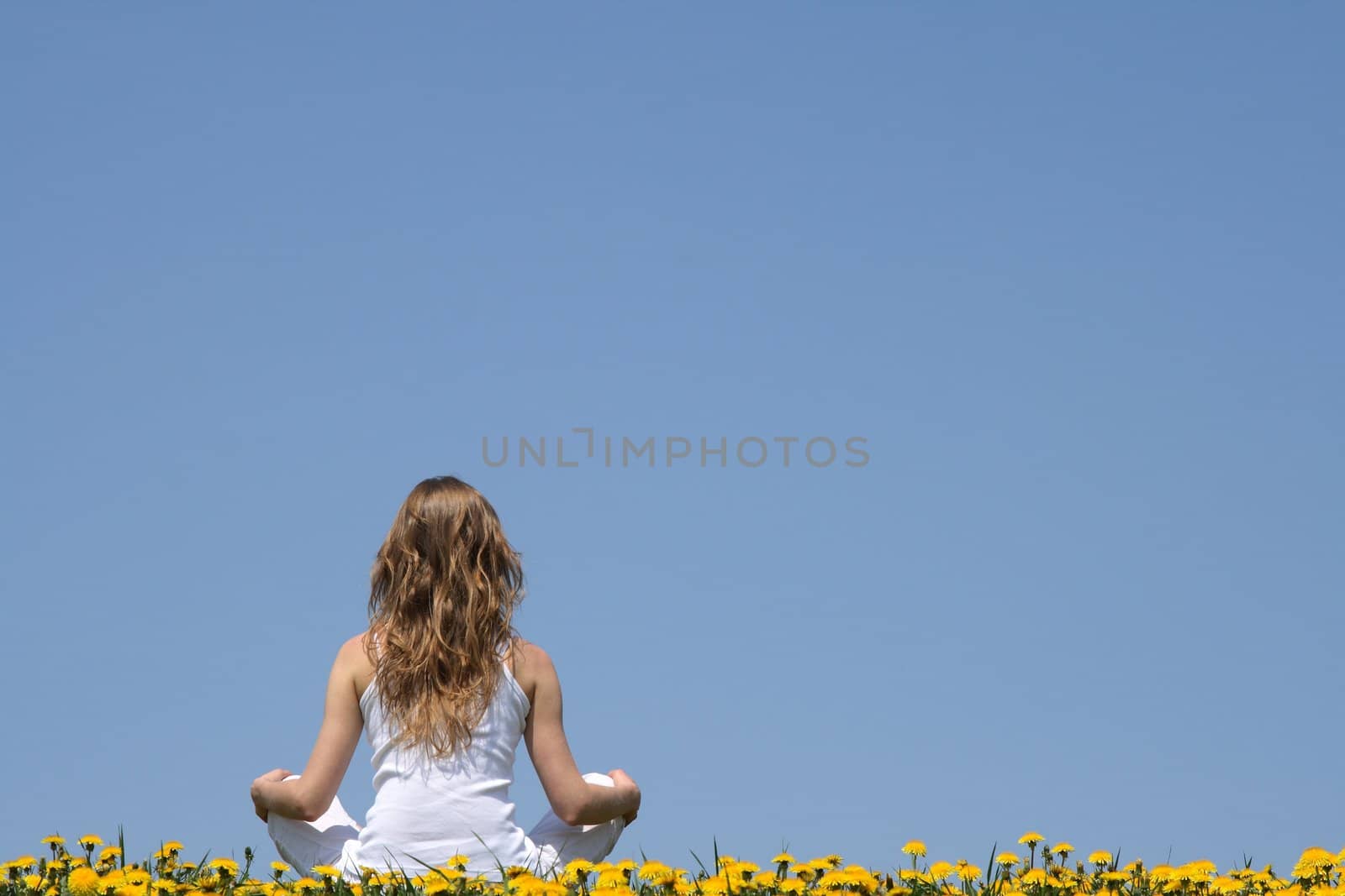Inner peace. Longhaired young woman in white clothes sitting in a flowering dandelion field.