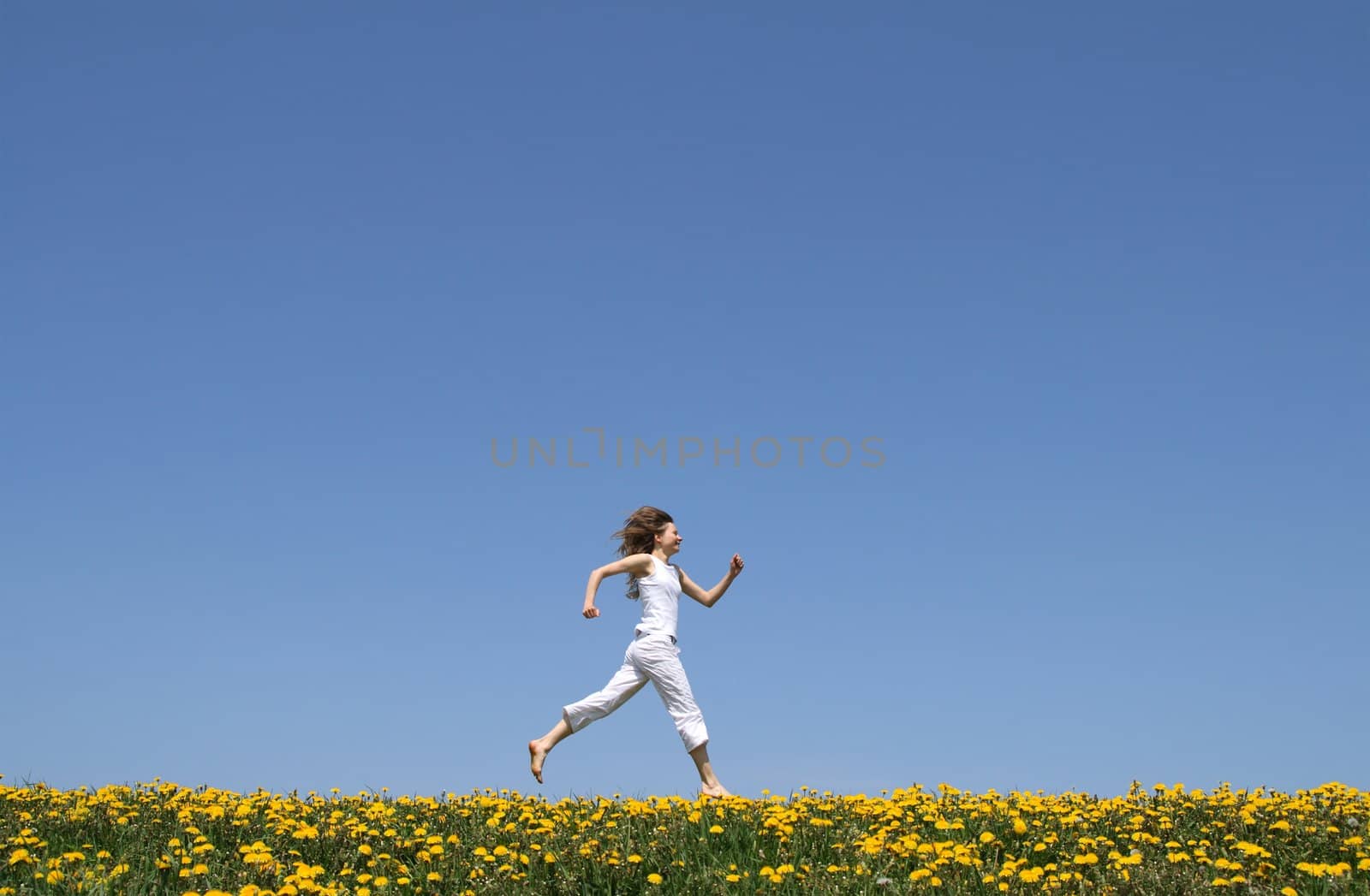 Happy girl in summer white clothes running in a flowering dandelion field.