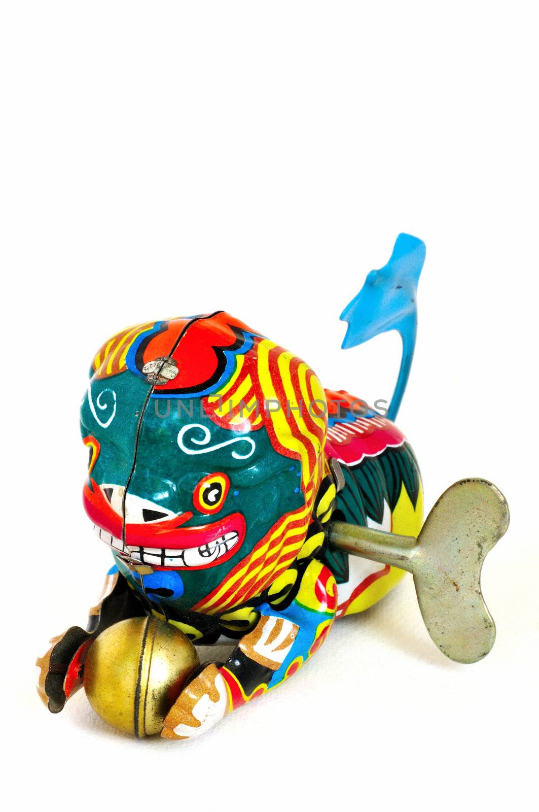 Wind-up toy dragon from China with blue tail and a golden ball in its paws, made of brightly-painted metal.  The winding key is visible in its side.