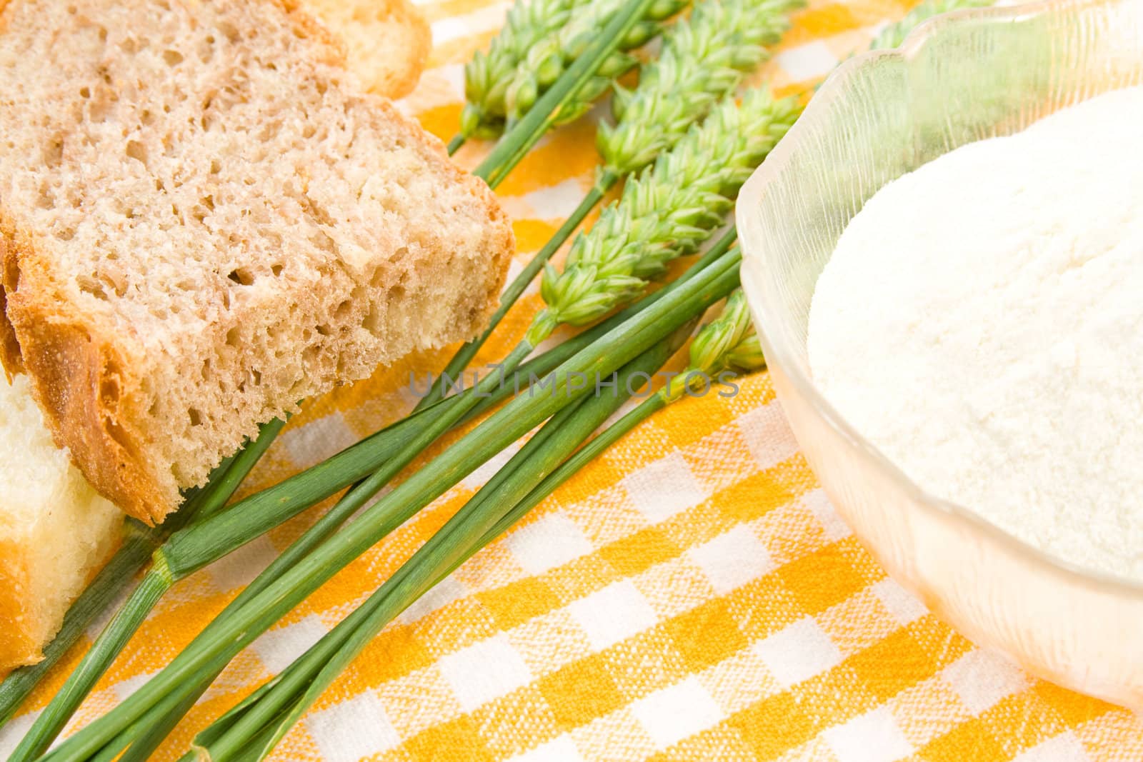 Bread, flour and green wheat on table cover.