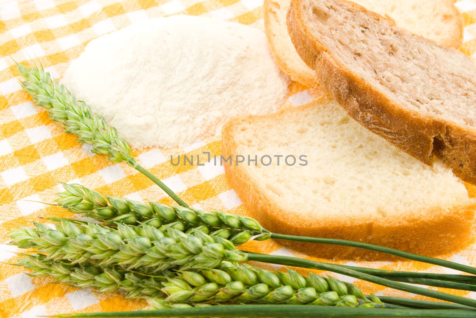 Bread, flour and green wheat on table cover.