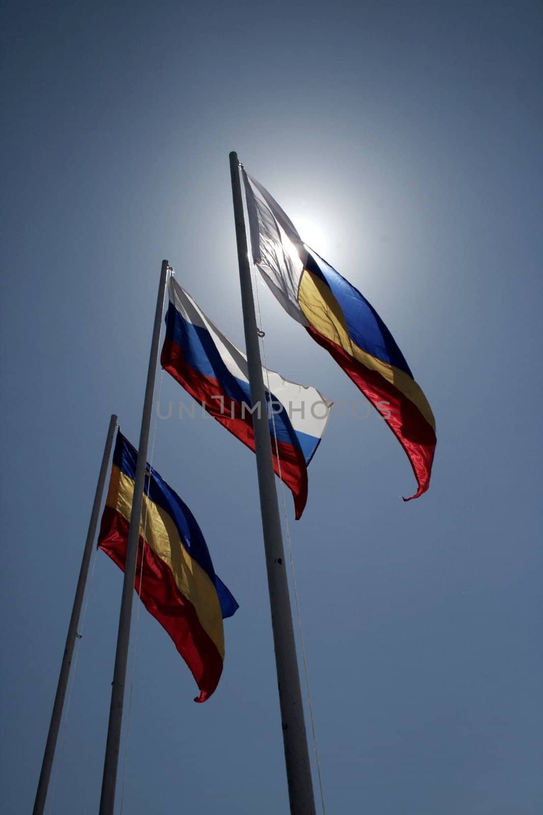 Three flags on sky and sun background.