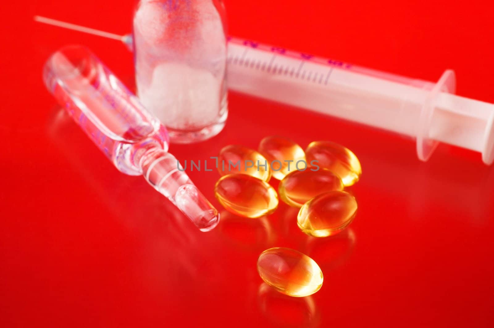 Syringe with pills and medicine bottles on red background