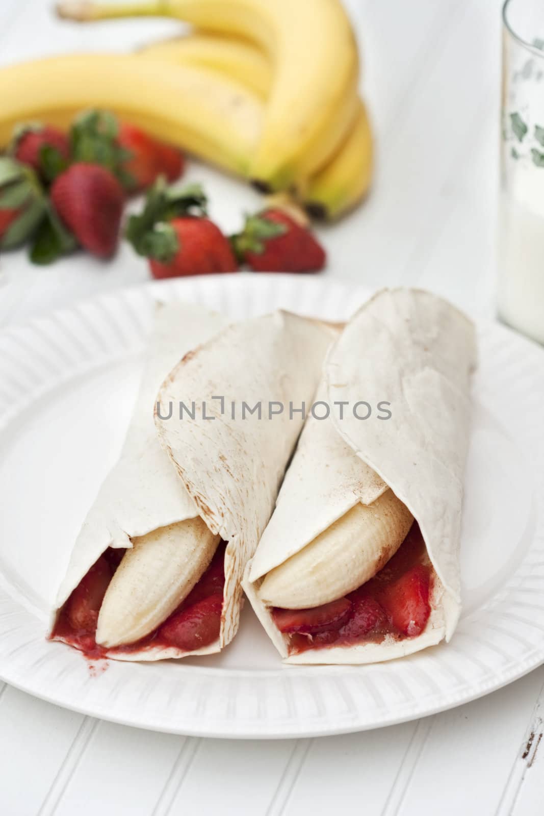 Banana and strawberry burritos on a rustic white table. Shallow DOF with focus on filling of burritos. 