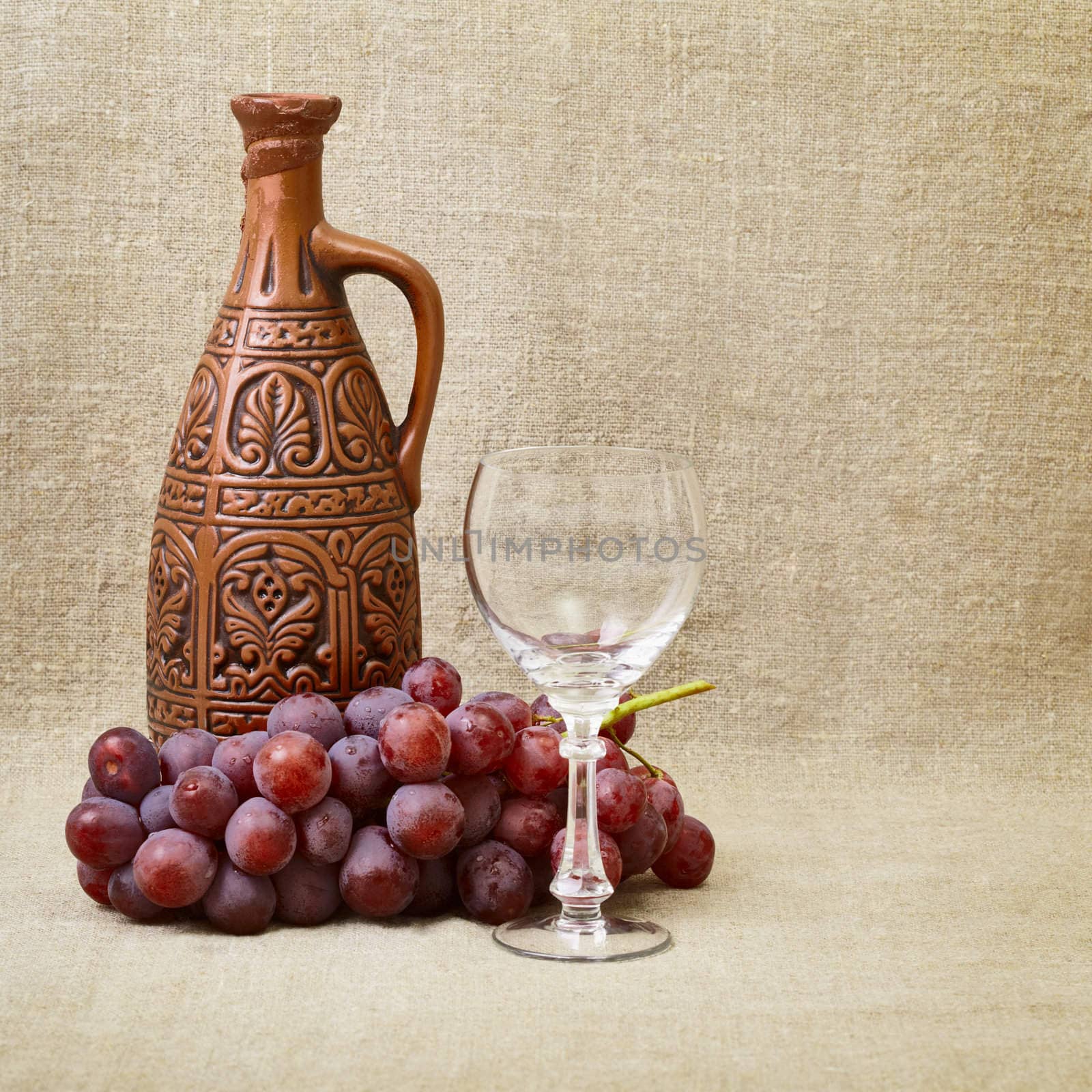 Still-life - clay bottle, grapes and a glass on the background of canvas