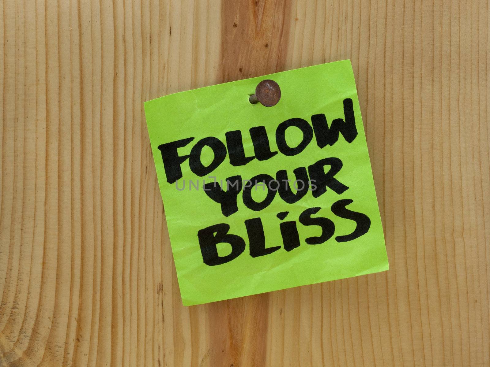 follow your bliss handwriting on a green sticky note nailed to wooden wall or plank