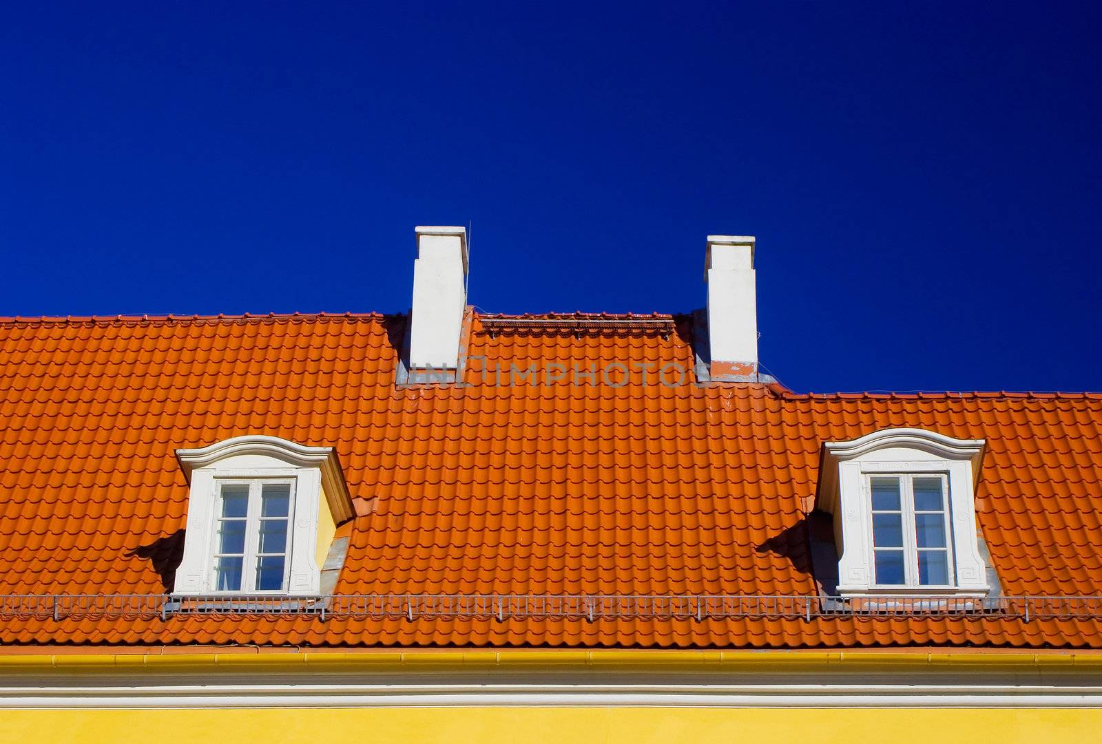 Orange roof with two windows and chimneys against blue sky