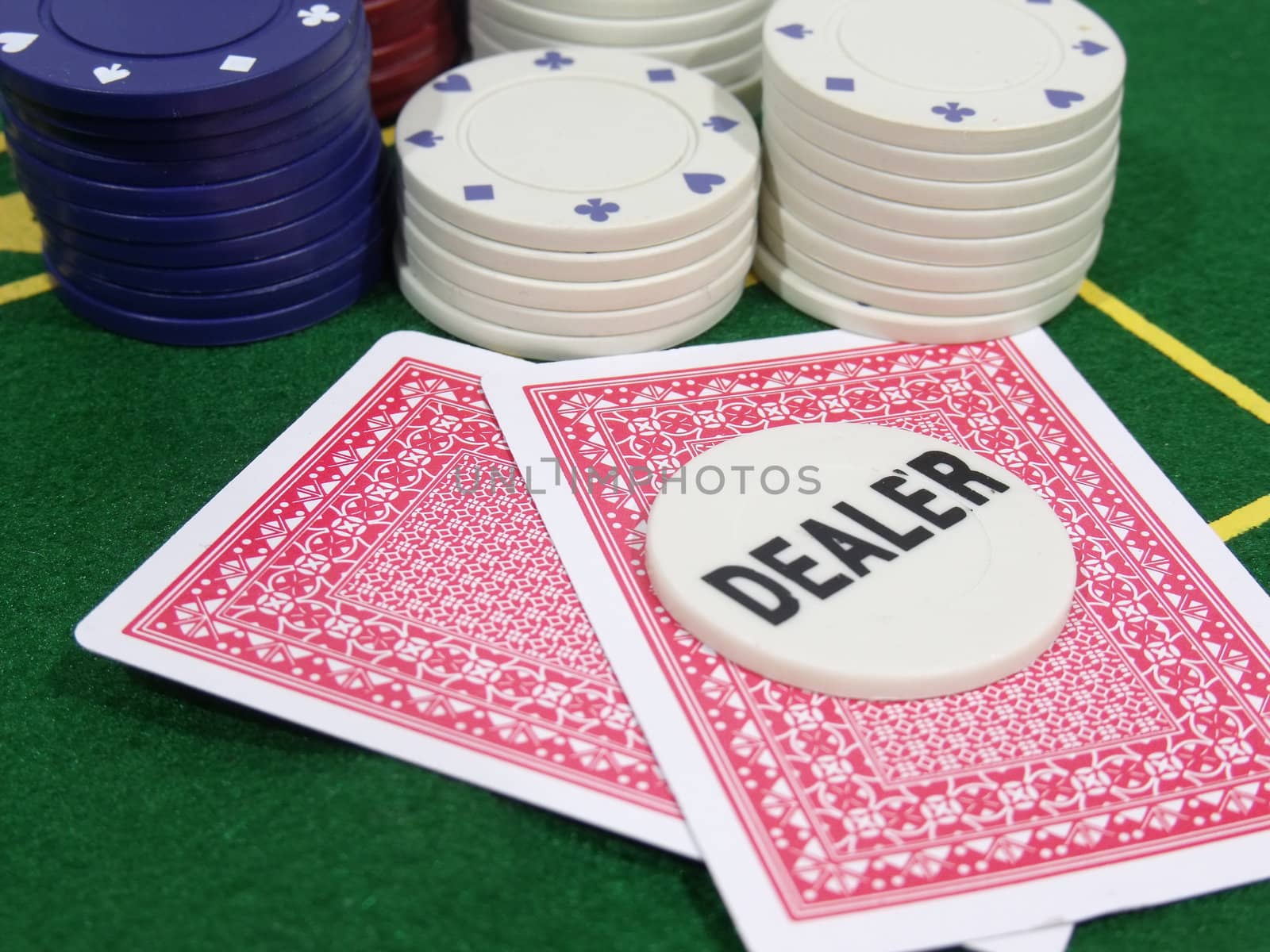 White poker dealer chip lying on two red playing cards