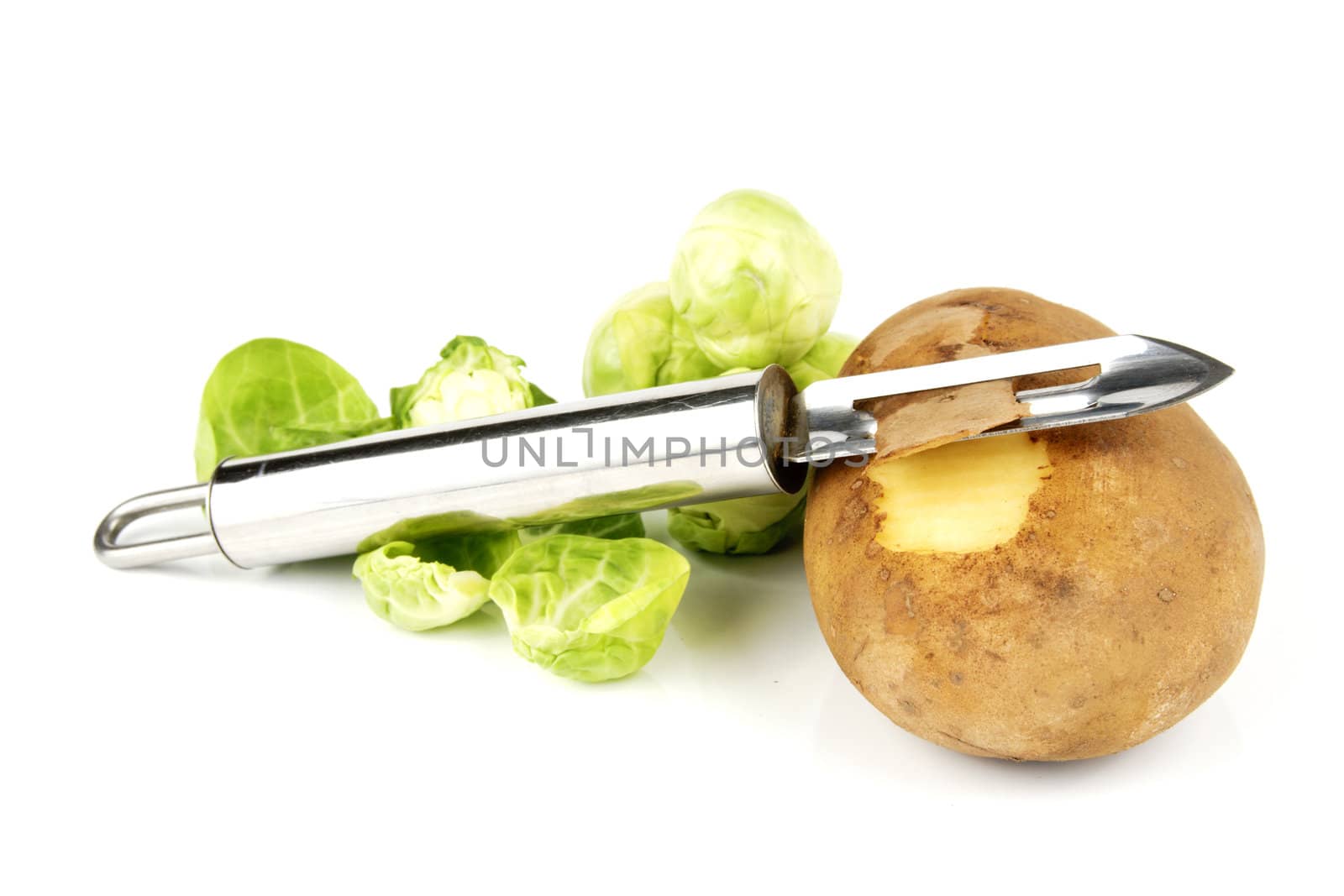 Small brown raw potato with chrome peeler and peeled green sprouts on a reflective white background