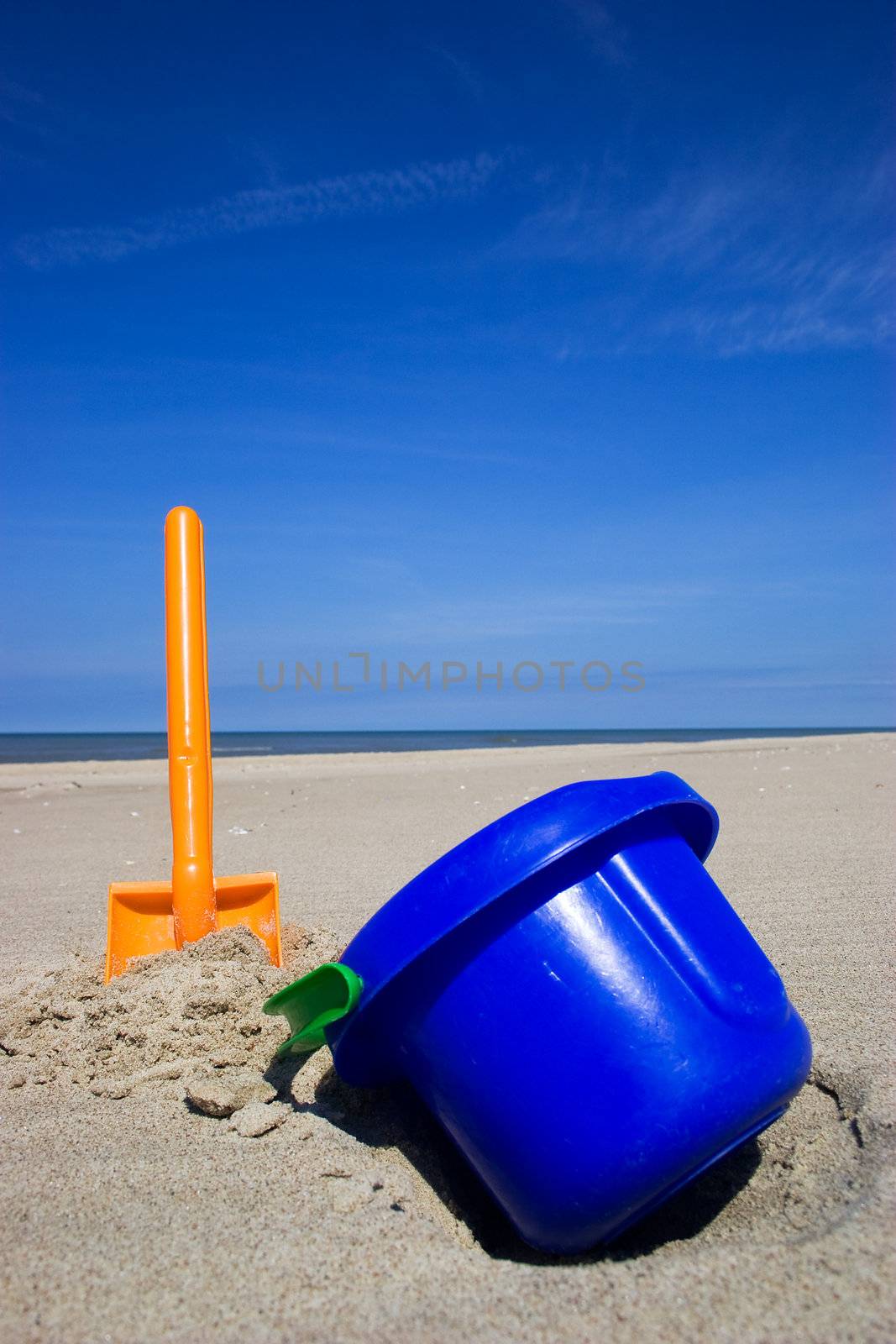 Orange plastic spade and blue bucket in the sandy seashore