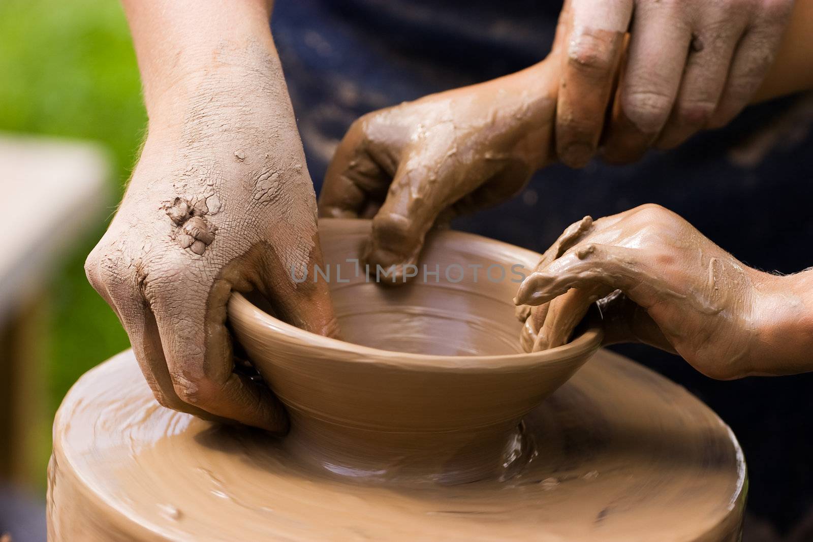 A potters hands guiding a child hands to help him to work with the ceramic wheel