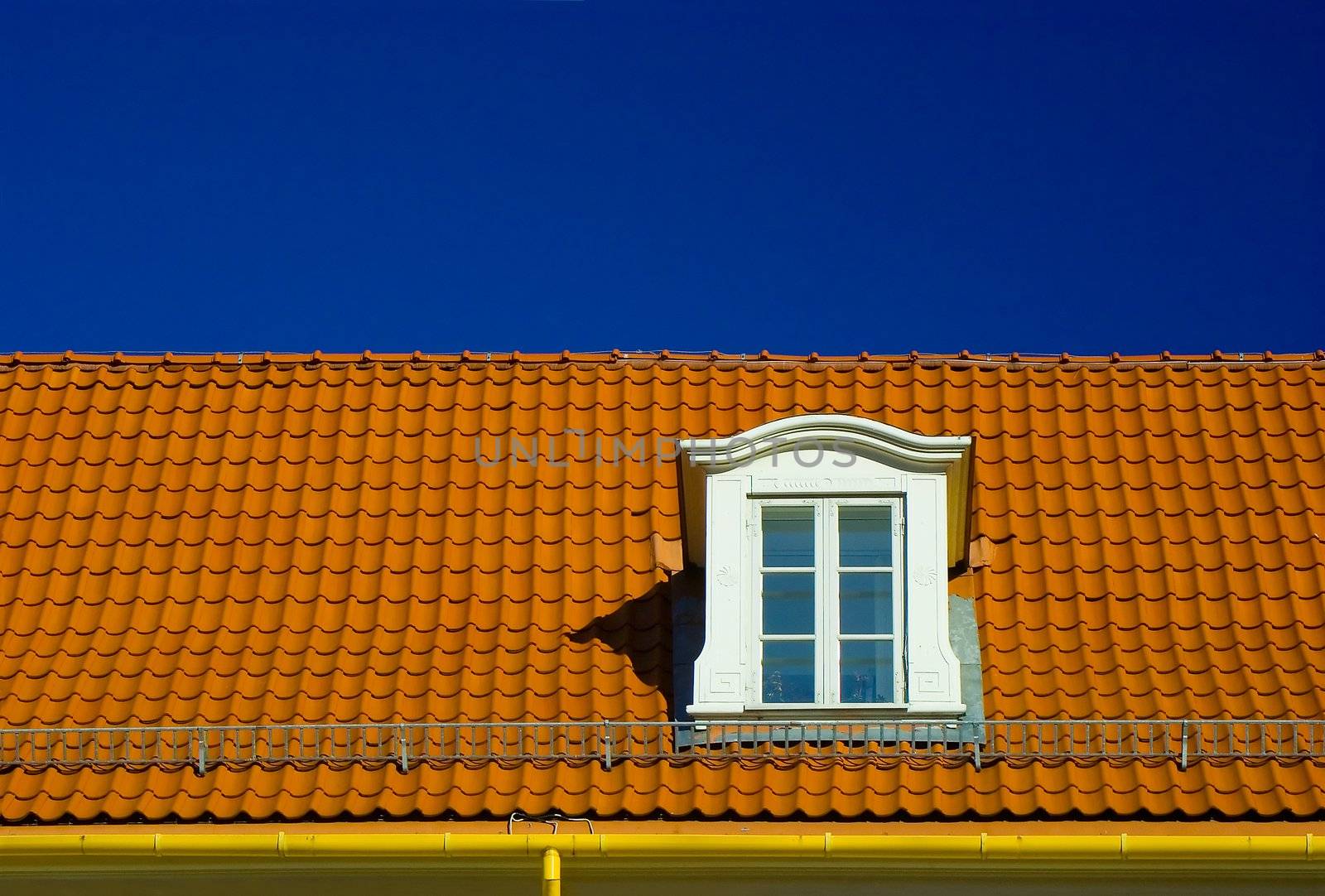 Dormer roof window, in a flashing orange tiled roof on blue sky