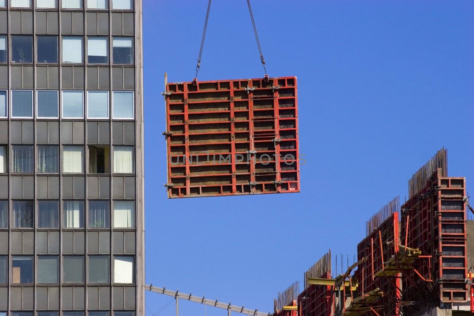 Tower crane lifting heavy red concrete frame