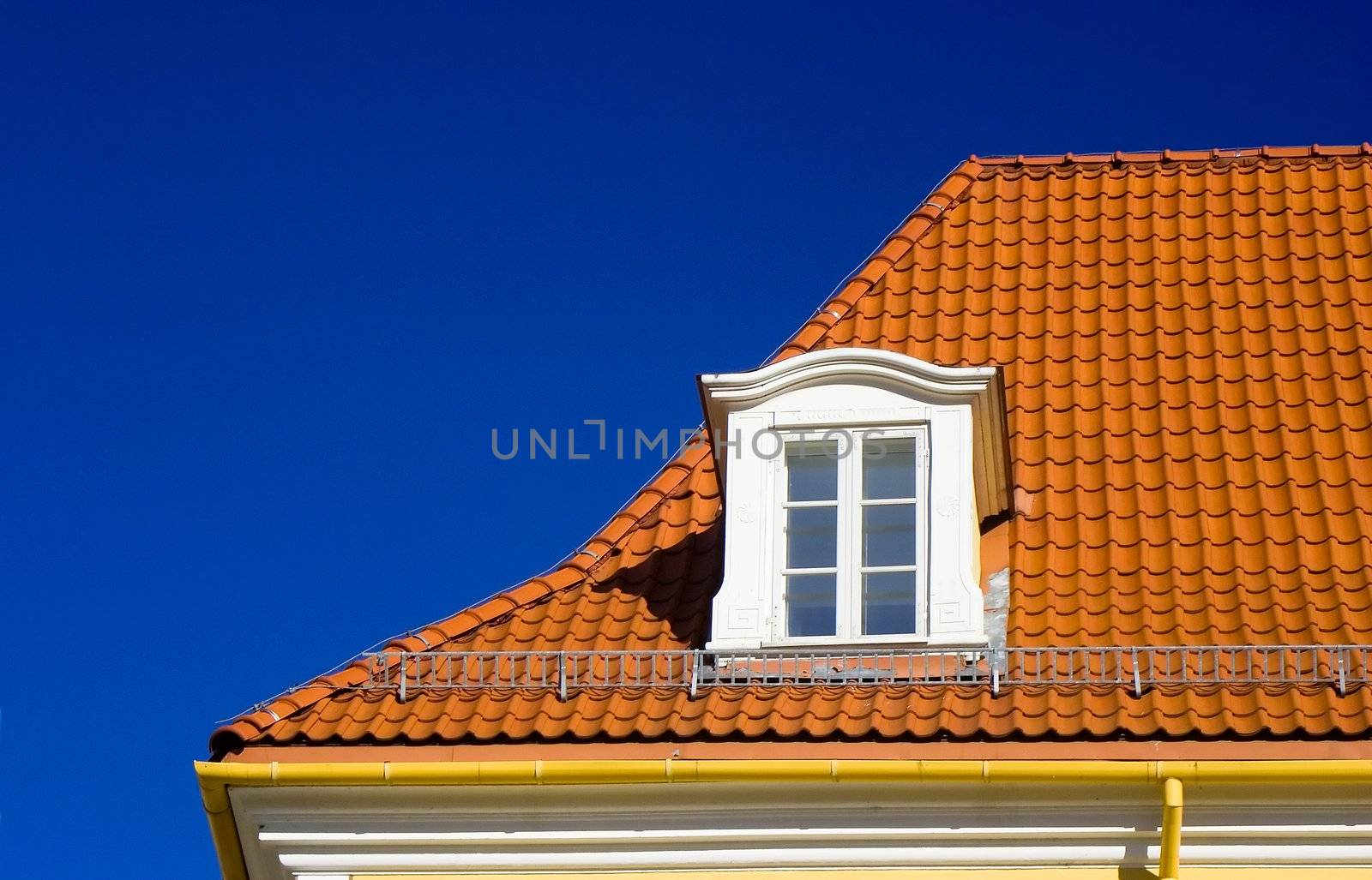 Flashing orange tiled roof on blue sky and one garrret window in Riga old town, Latvia