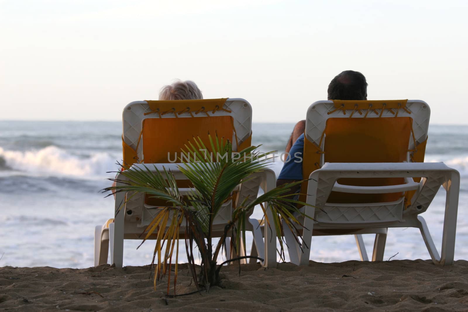 couple lying in chaise longues on the beach by hotel