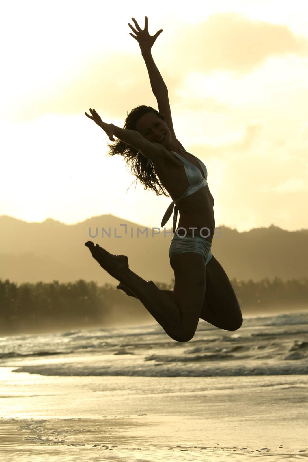 Woman in silver bikinis jumps on the beach by sunset