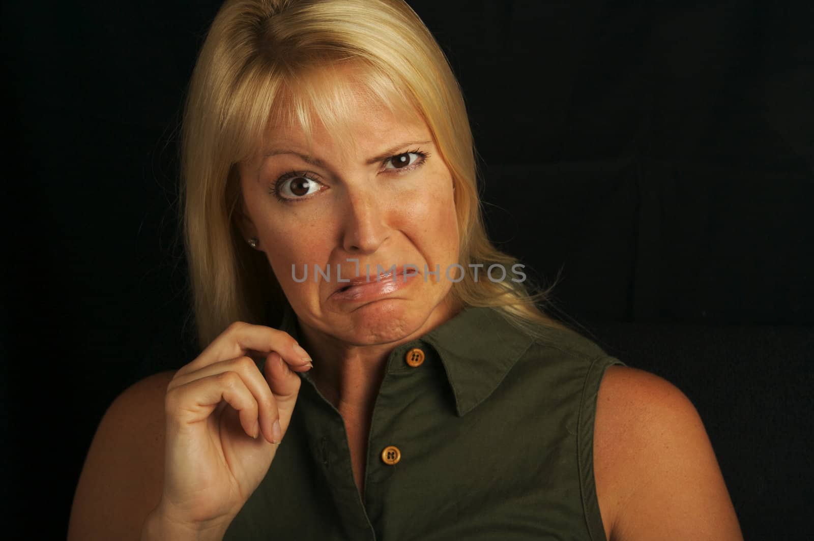 Attractive Blond Haired, Brown Eyed Woman Grimaces on a black background.