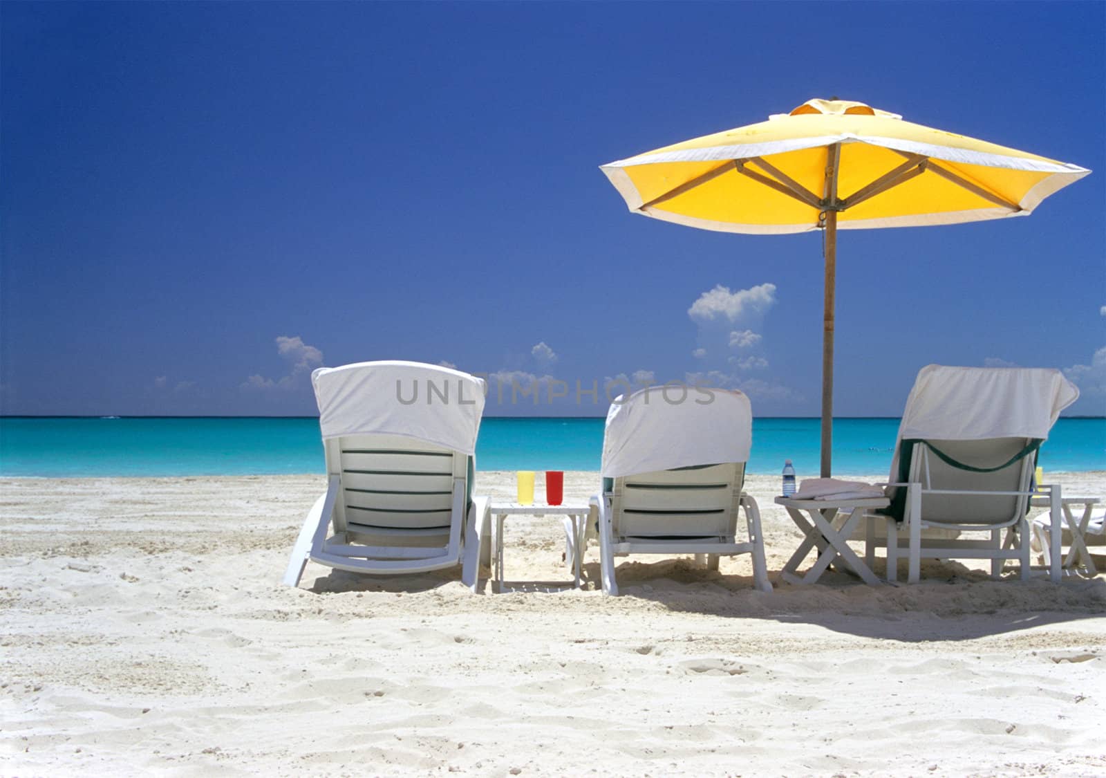 Empty deck chairs wait on a white sandy beach facing the turquoise waters of the Bahamas.