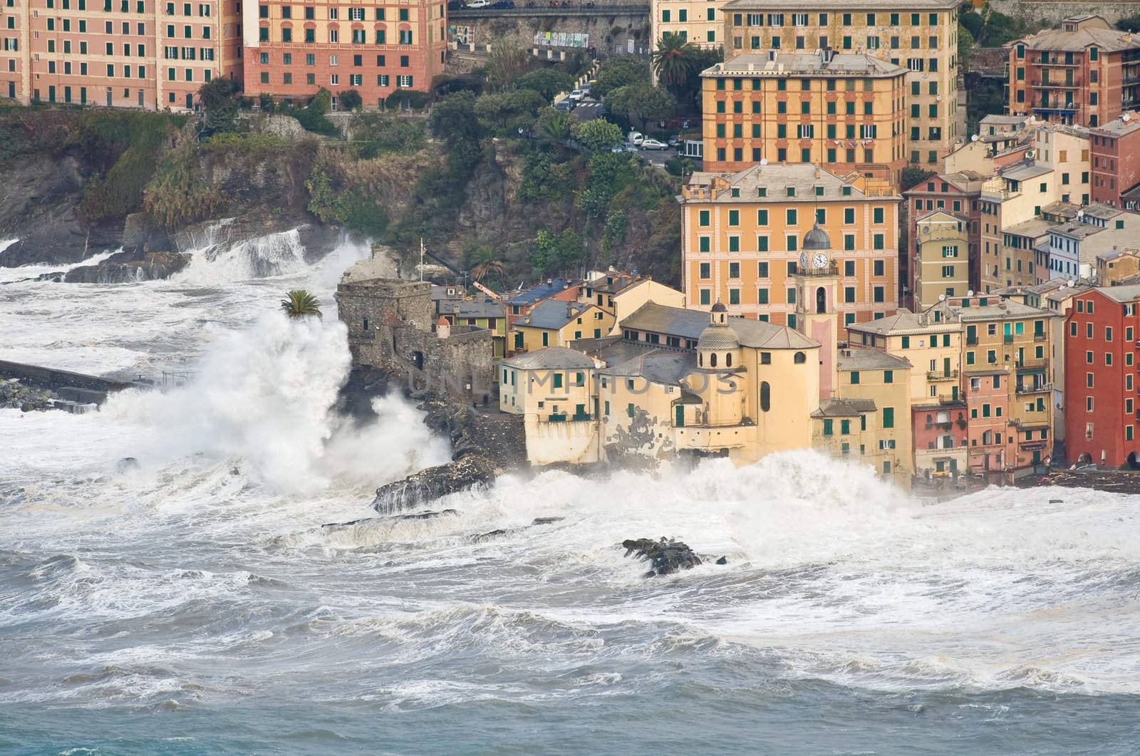 Waves break over the church and the castle in Camogli, Italy