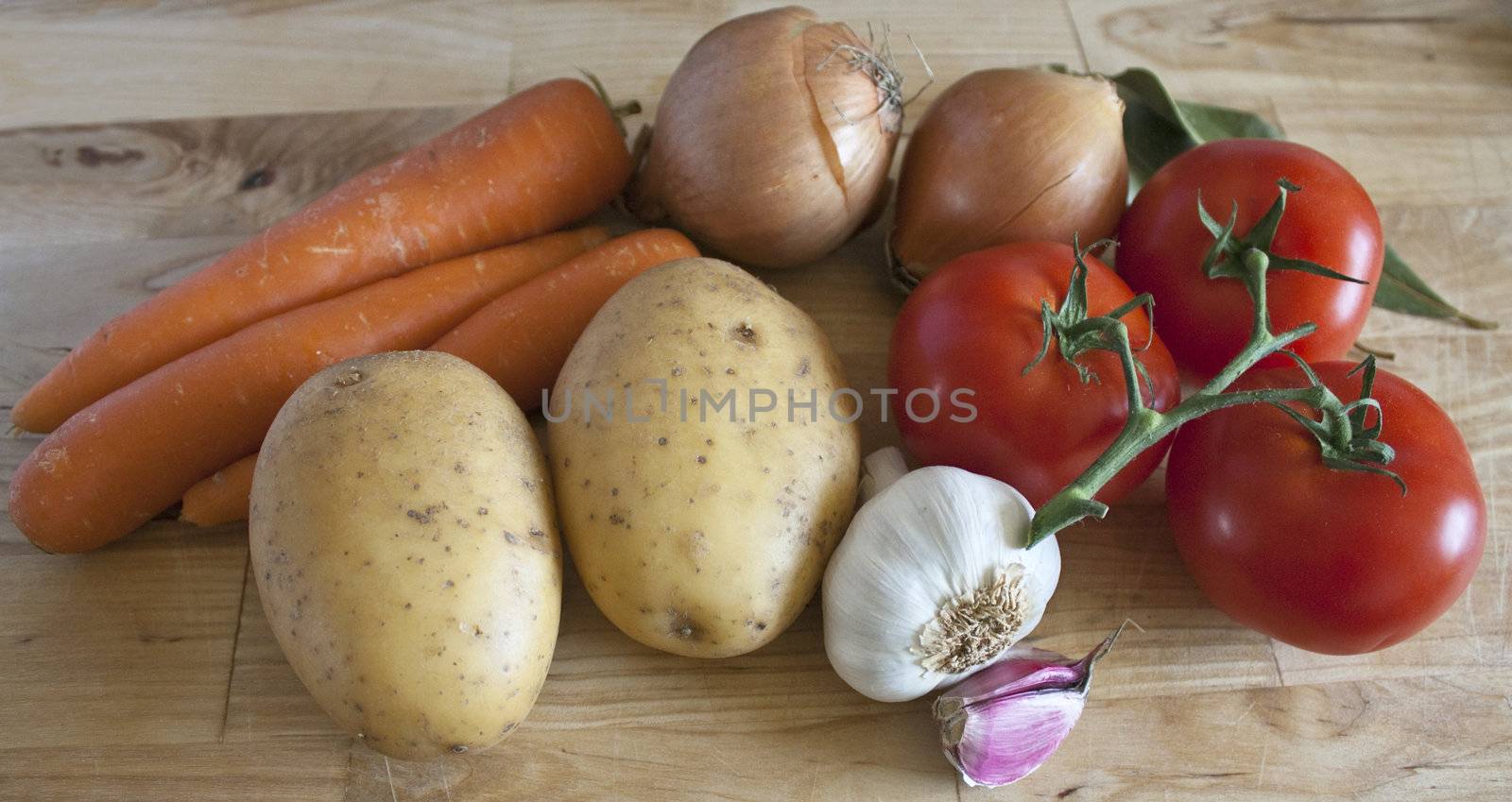 Some carrots, potatoes, onions, tomatoes, garlic and laurel on chopping board.