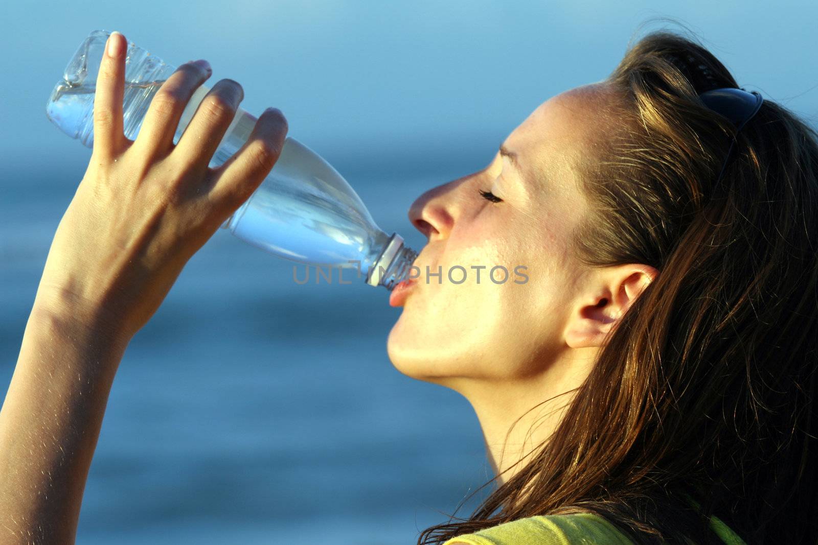woman drinking water from bottle by the beach