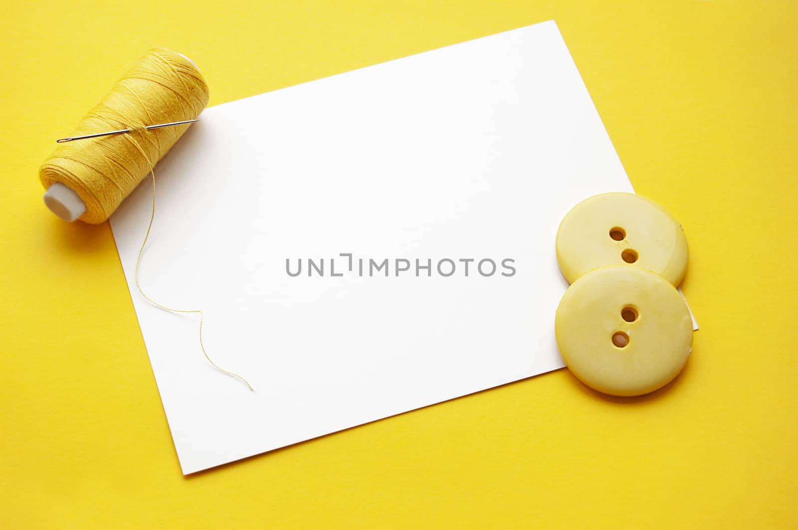 Yellow thread, needles and some buttons on blank note