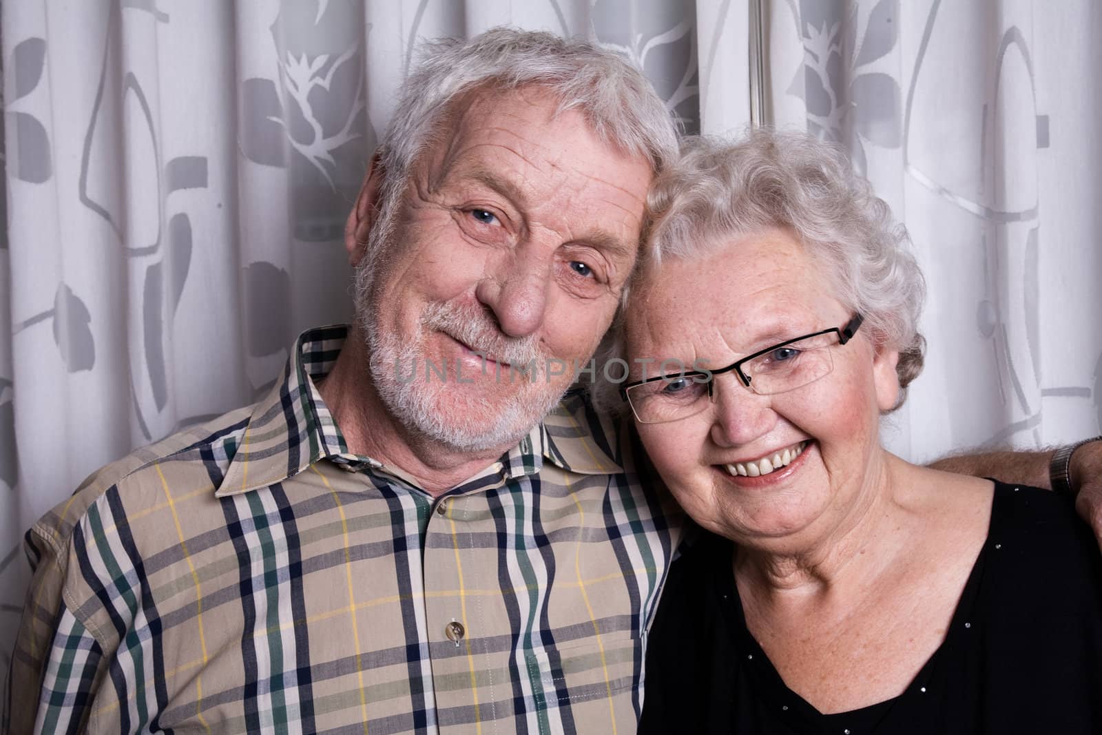 portrait of an elderly couple posing in front of curtains