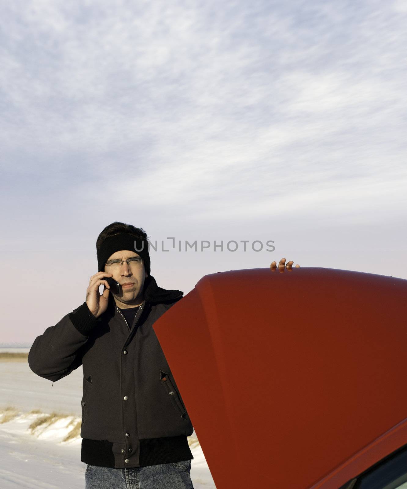 A young man is checking under the car hood while talking on a cell phone. Copyspace available.