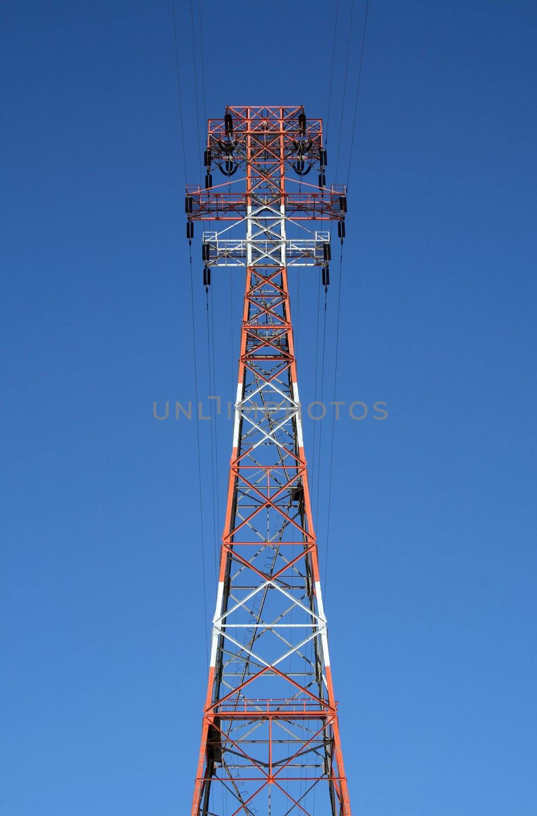 Top of the red and white high voltage power tower against the blue sky.