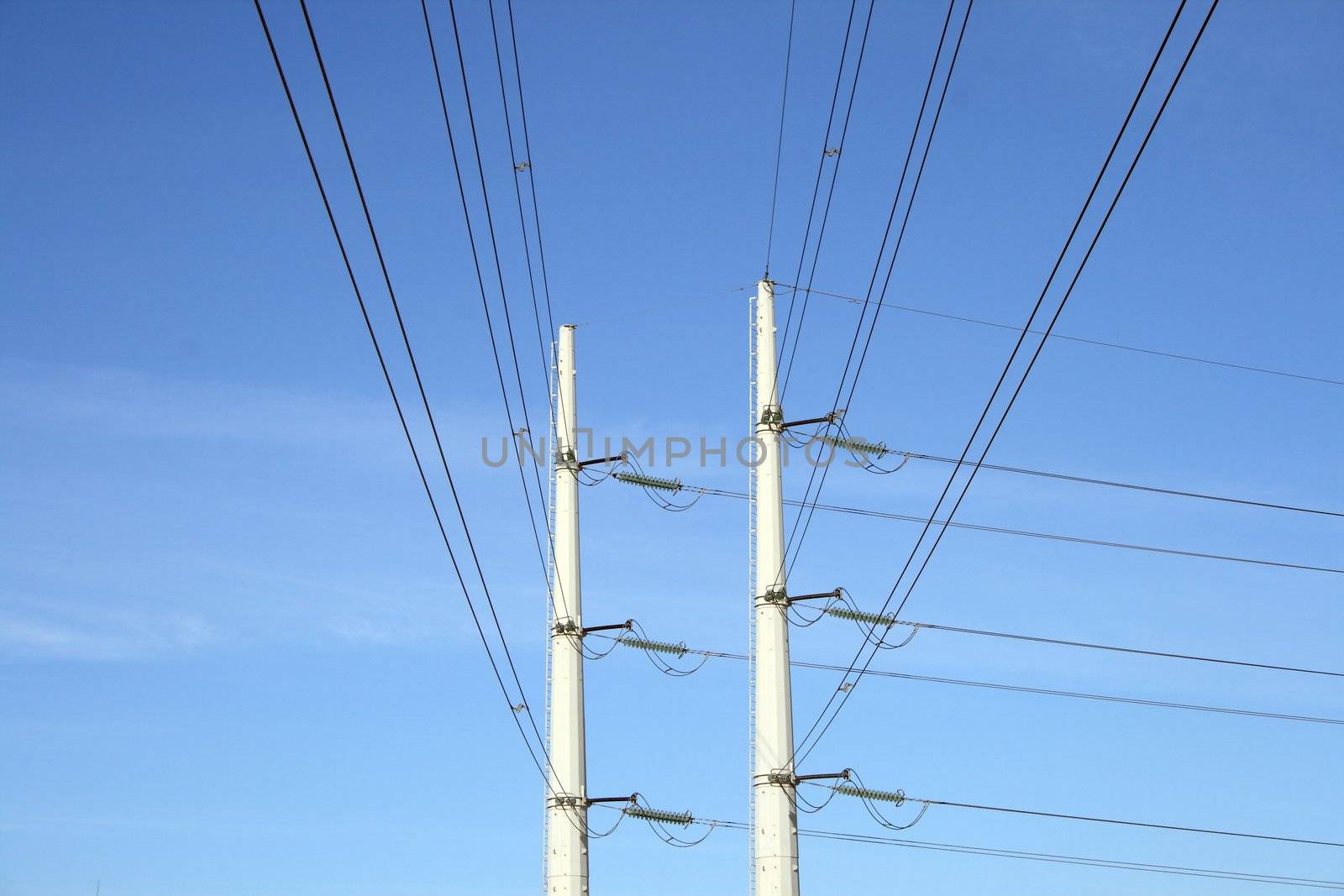 Two white electricity pylons, and wires stretching against the blue sky.