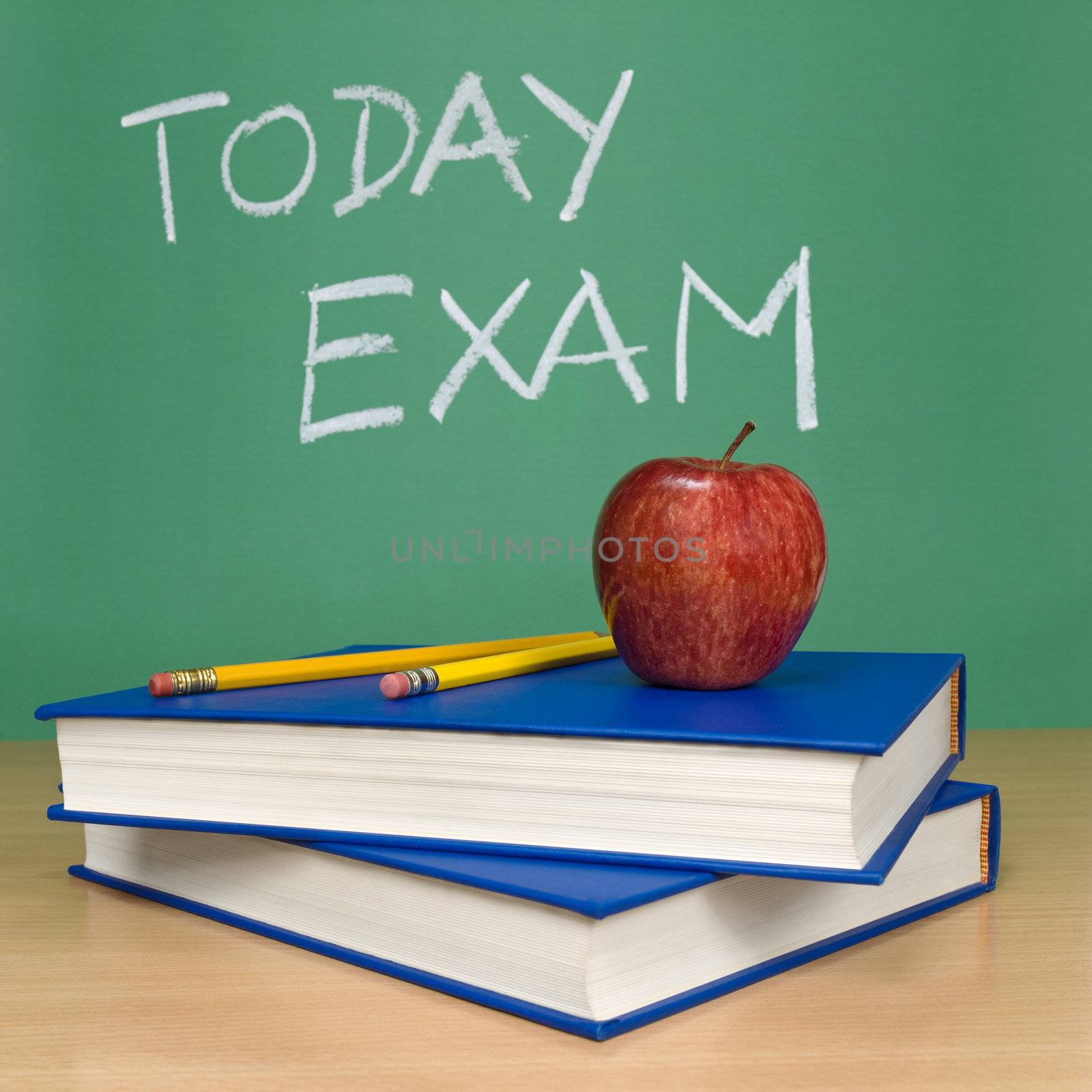 Today exam written on a chalkboard. Books, pencils and an apple on foreground.