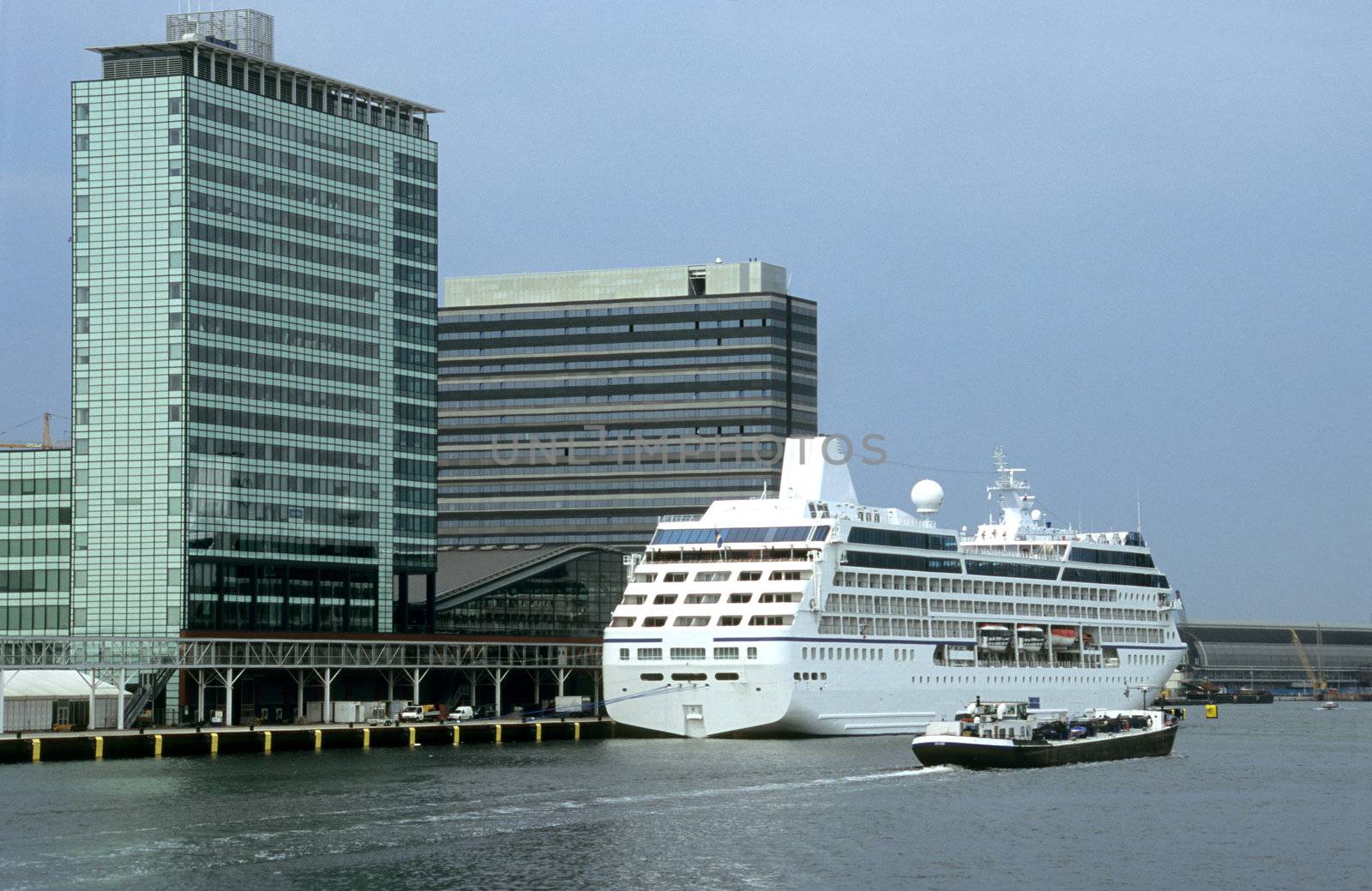 A cruise ship docks at Amsterdam's new harbor on the Ij canal, behind Centraal Station as a barge passes by.