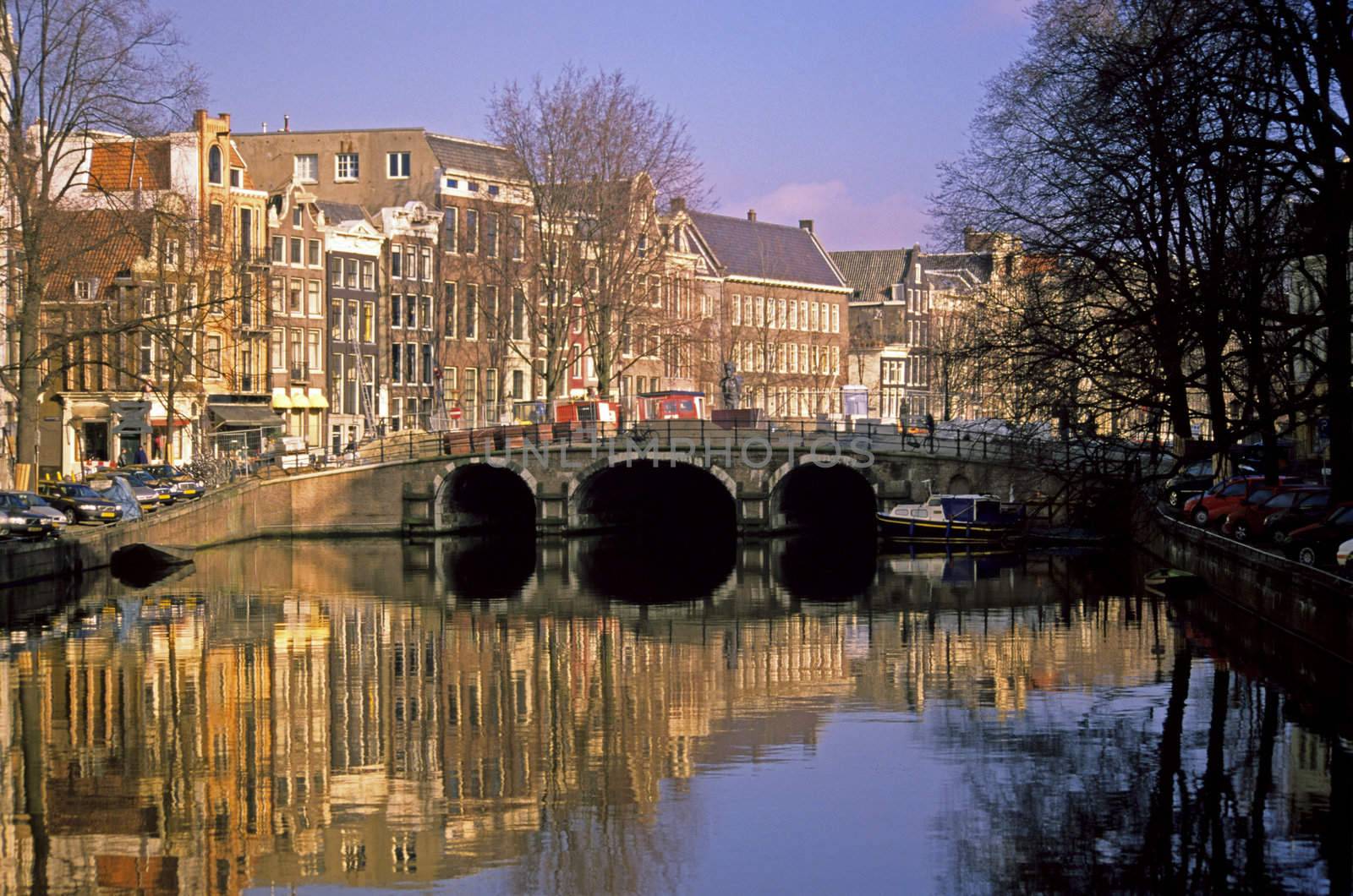 Traditional canal houses line a canal spanned by a scenic bridge in Amsterdam, the Netherlands.