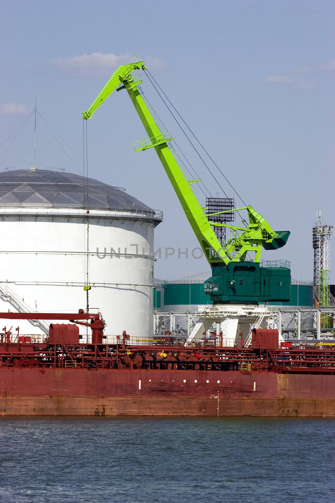 Green port crane working. White cylindrical tanks for industrial chemicals and petroleum products in background
