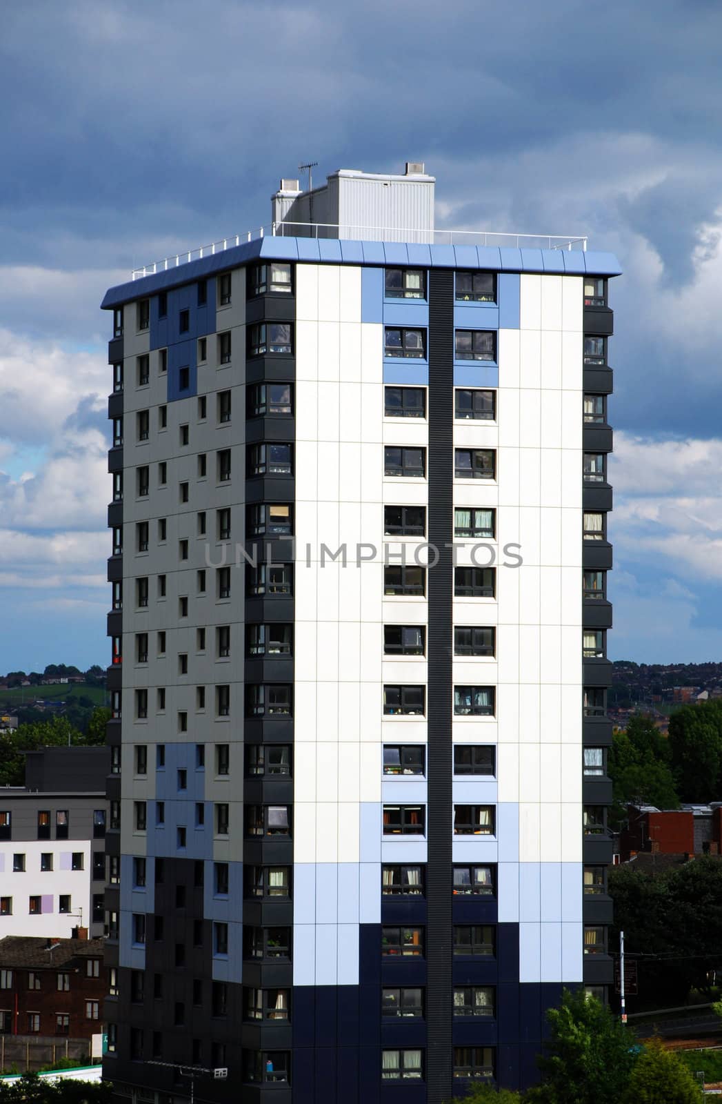 A photograph of a tall, cladded block of flats underneath an imposing, cloudy sky