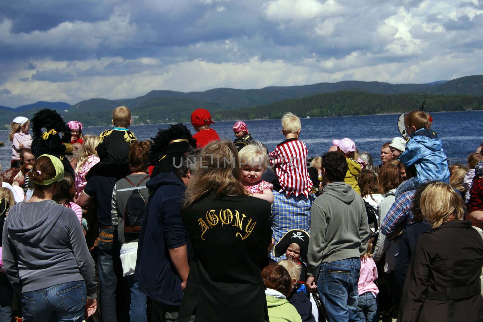crowd of people at a pirat gathering in Holmestrand, Norway, a man holding a toddler, his jacket has the word agony formed on the back.