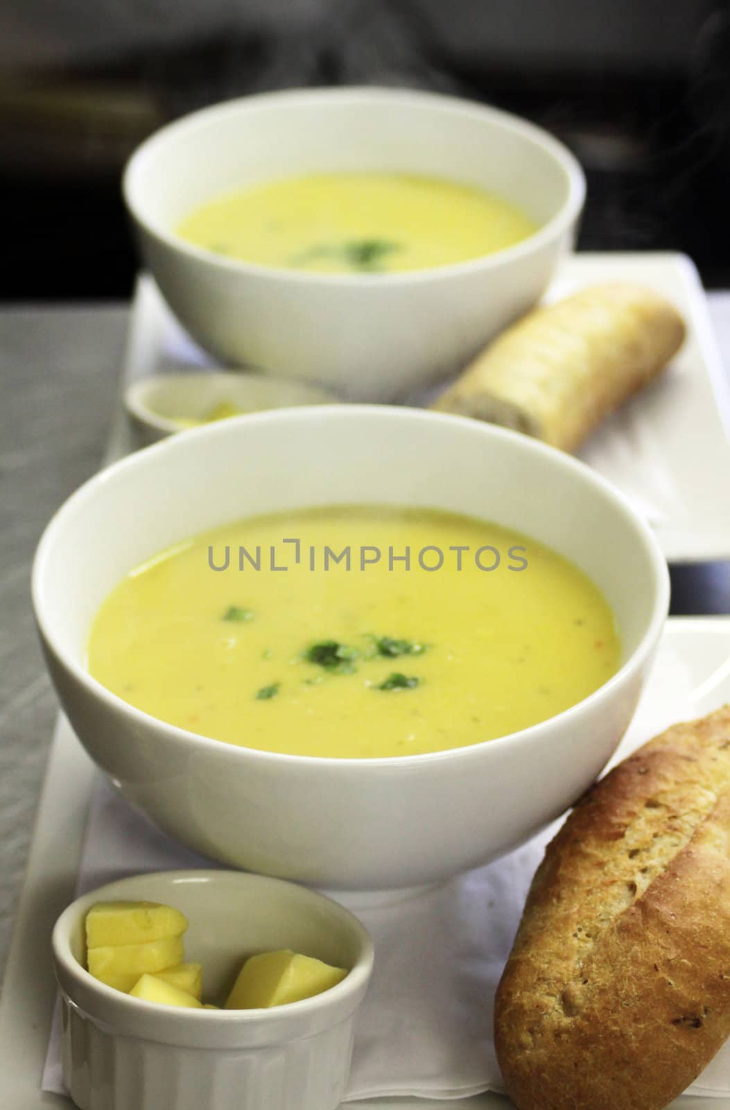 Two bowls of freshly made parsnip soup in white bowls on a tray set with a ramakin of butter and fresh crusty bread.