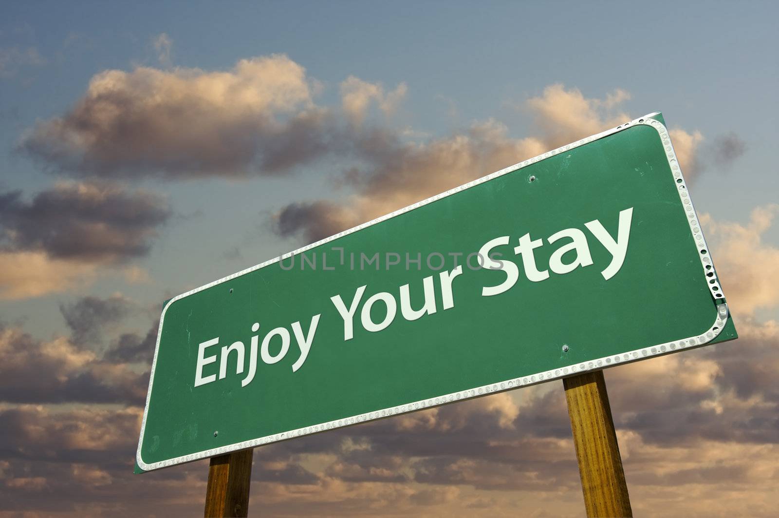 Enjoy Your Stay Green Road Sign with dramatic clouds and sky.