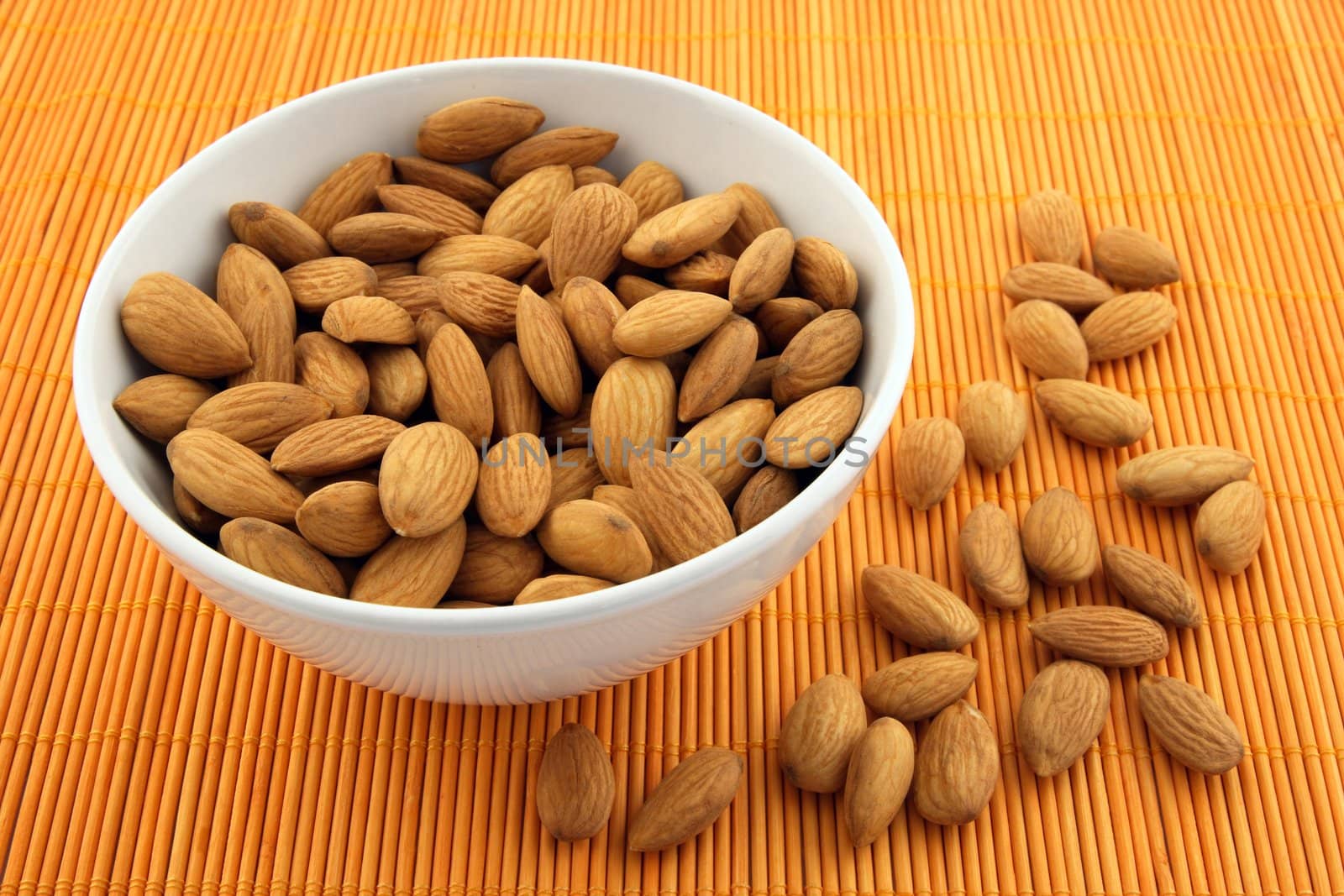 Bowl full of fresh almonds on warm orange background.